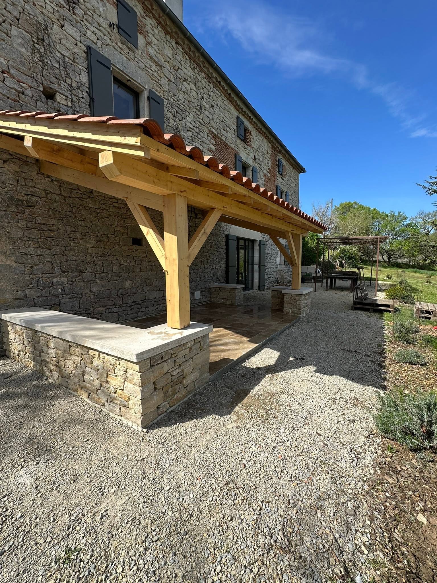 Auvent en bois sur une terrasse avec murets en pierre
